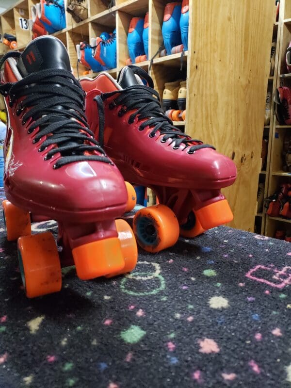 A pair of red roller skates on top of a black and orange carpet.