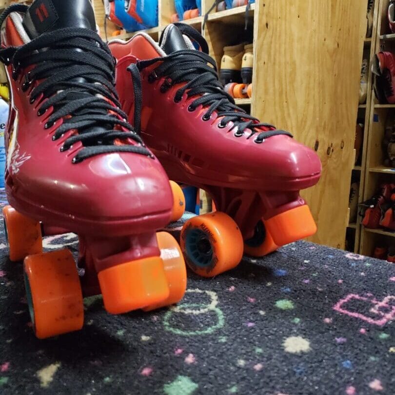 A pair of red roller skates on top of a black and orange carpet.